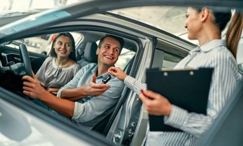 Beautiful happy couple bought a car in the dealership and receives the keys from the manager.